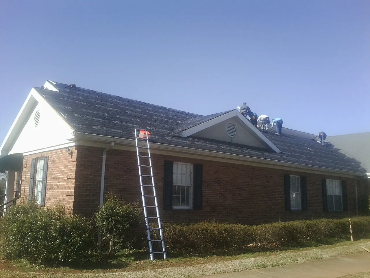 Crew tearing shingles off a brick ranch roof with a ladder set — Metal Roof Repair work by our crew in Bremen