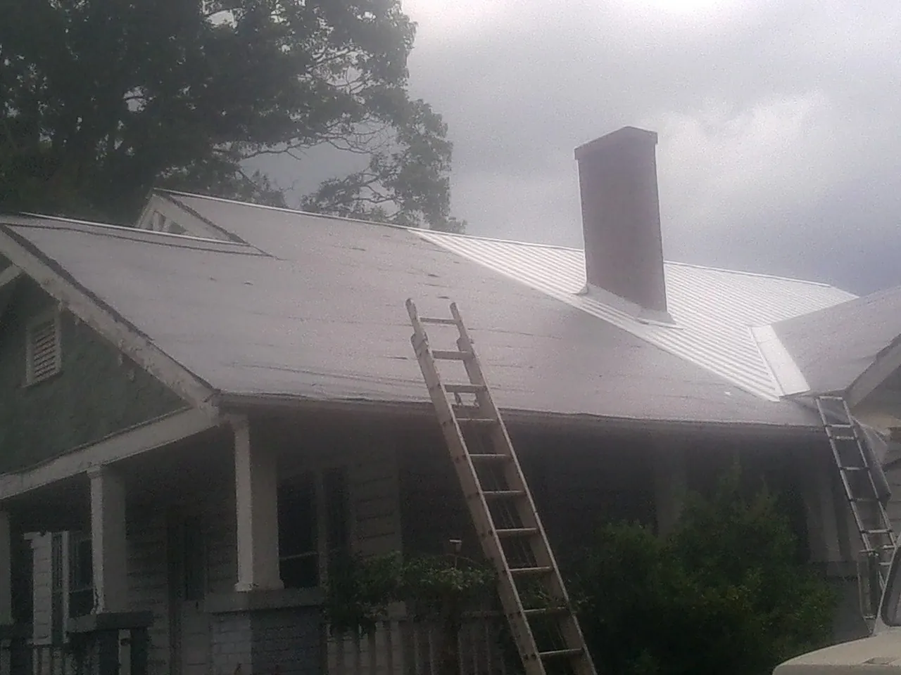 Ladders against a metal roof on an older home with a brick chimney in Bremen
